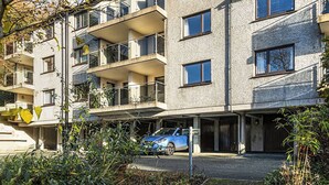 Un edificio residenziale a più piani con balconi, un'area di parcheggio e un'auto blu parcheggiata di fronte.