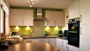 Una cucina moderna con mobili bianchi, un'isola ampia con posti a sedere, forno a incasso e parete di fondo verde.