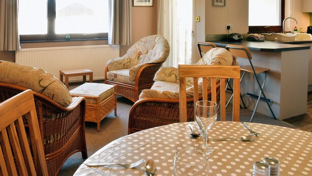 Un soggiorno accogliente con mobili in vimini, un tavolo da pranzo con tovaglia a pois e un angolo cottura con lavello e piano di lavoro.