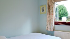 Camera da letto con un letto singolo, una finestra con tende floreali, un quadro appeso e un termosifone.