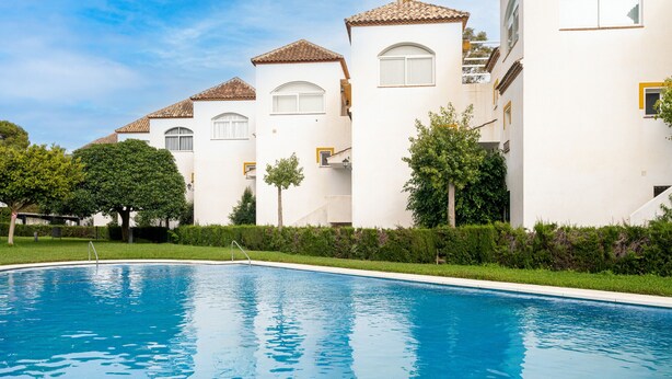Una piscina rodeada de edificios blancos con tejados de cerámica y pequeños árboles.