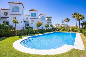 Una piscina rodeada de césped cuidado, con un edificio con múltiples ventanas y balcones al fondo.
