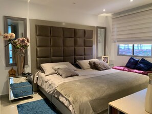 Une chambre à coucher moderne avec un grand lit, une table de chevet, un miroir et une fenêtre donnant sur la mer.