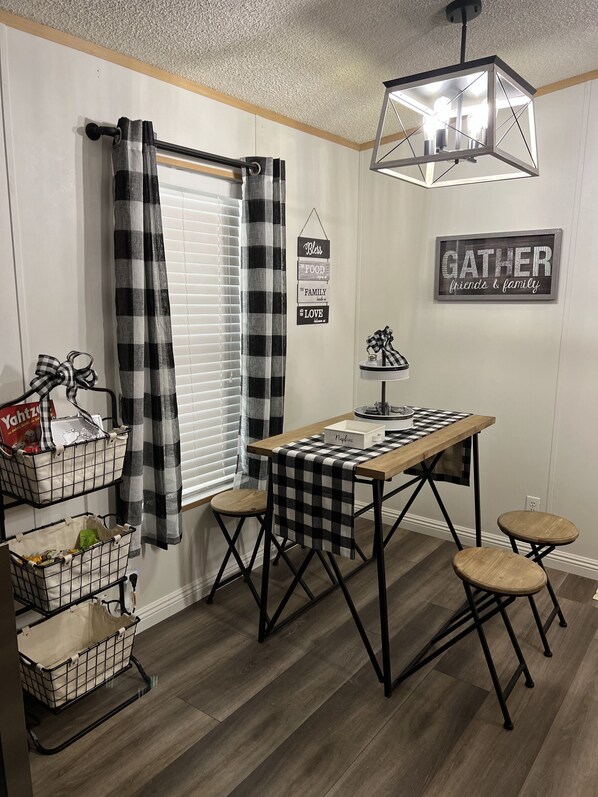 Un coin repas avec une nappe à carreaux, des chaises en métal noir et un luminaire suspendu.