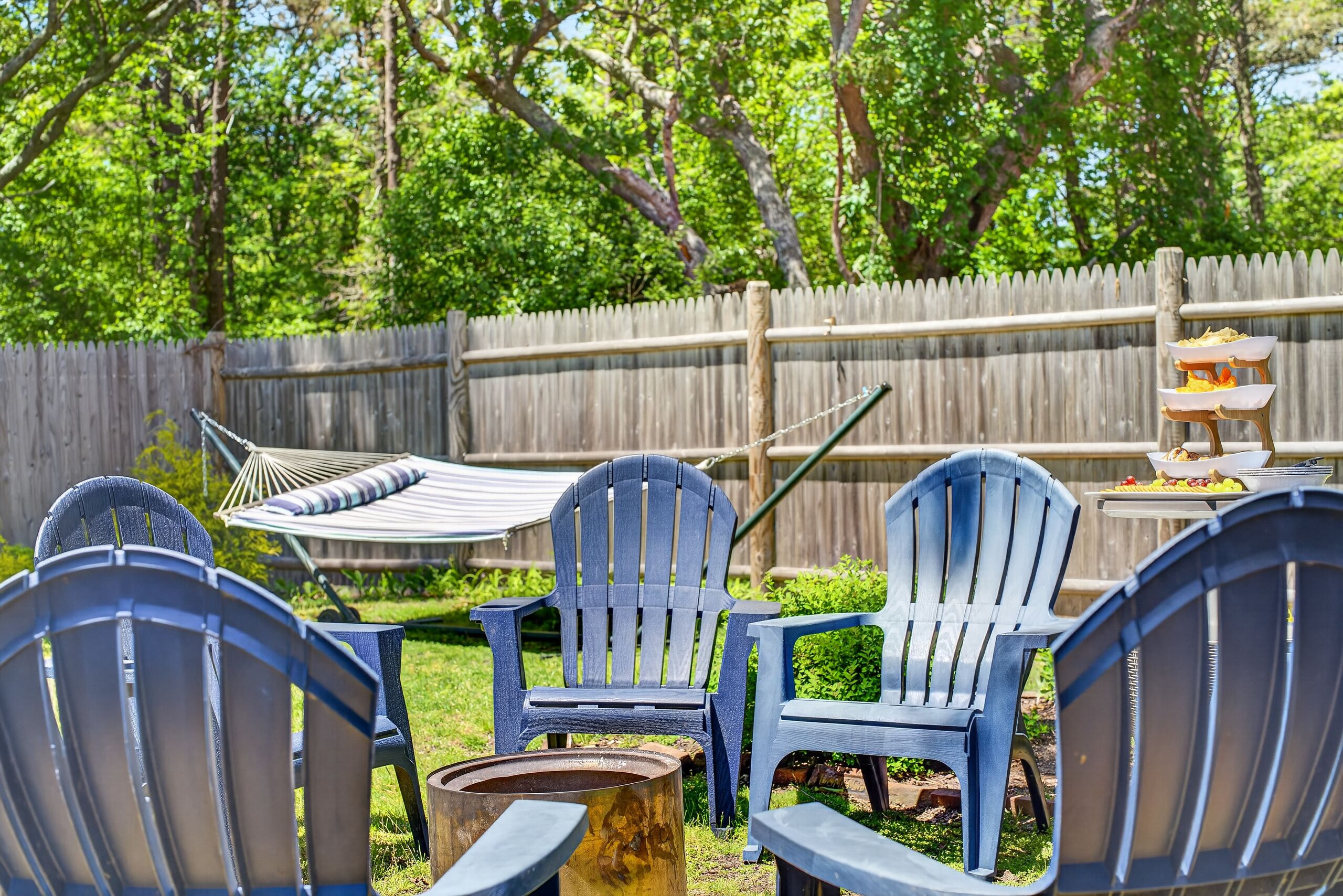 A backyard with a wooden fence, a hammock, and outdoor furniture including chairs and a table.