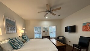 Une chambre à coucher comprenant un lit, un bureau, une chaise, un ventilateur de plafond, une télévision et des œuvres d’art accrochées aux murs.