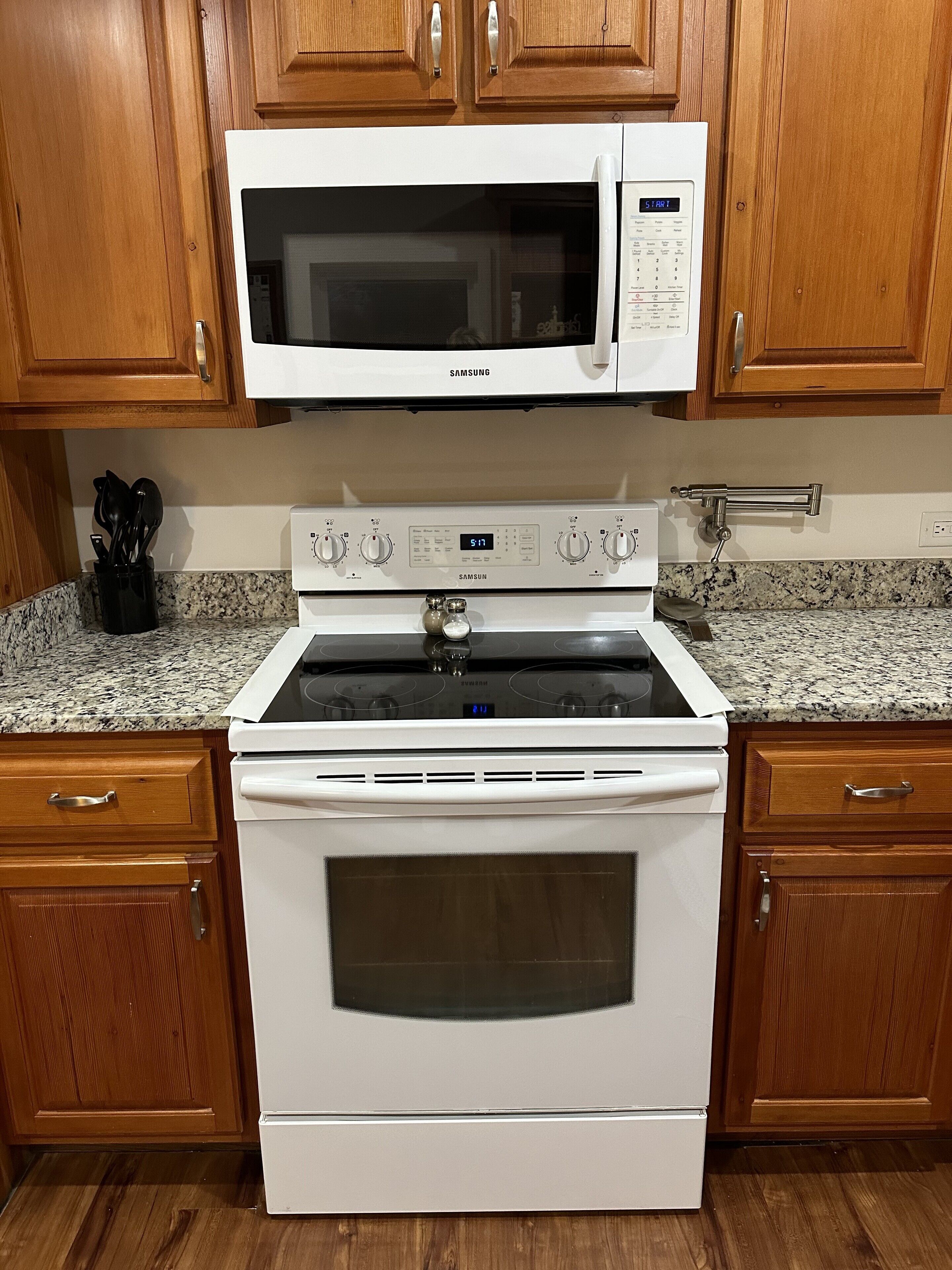 A kitchen with a white microwave, stove, and oven, wooden cabinets, and granite countertops.