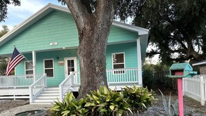 Une maison turquoise avec un porche, une nichoir et un drapeau.
