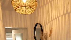 Un couloir avec une étagère en bois sur laquelle sont posés un miroir, un tableau encadré et des plantes séchées.