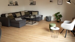Un salon moderne avec un canapé d’angle, une petite table ronde, un pouf vert et un fauteuil blanc.