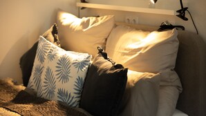 Un lit bien fait, agrémenté de plusieurs coussins, une lampe de chevet et une prise électrique au mur.