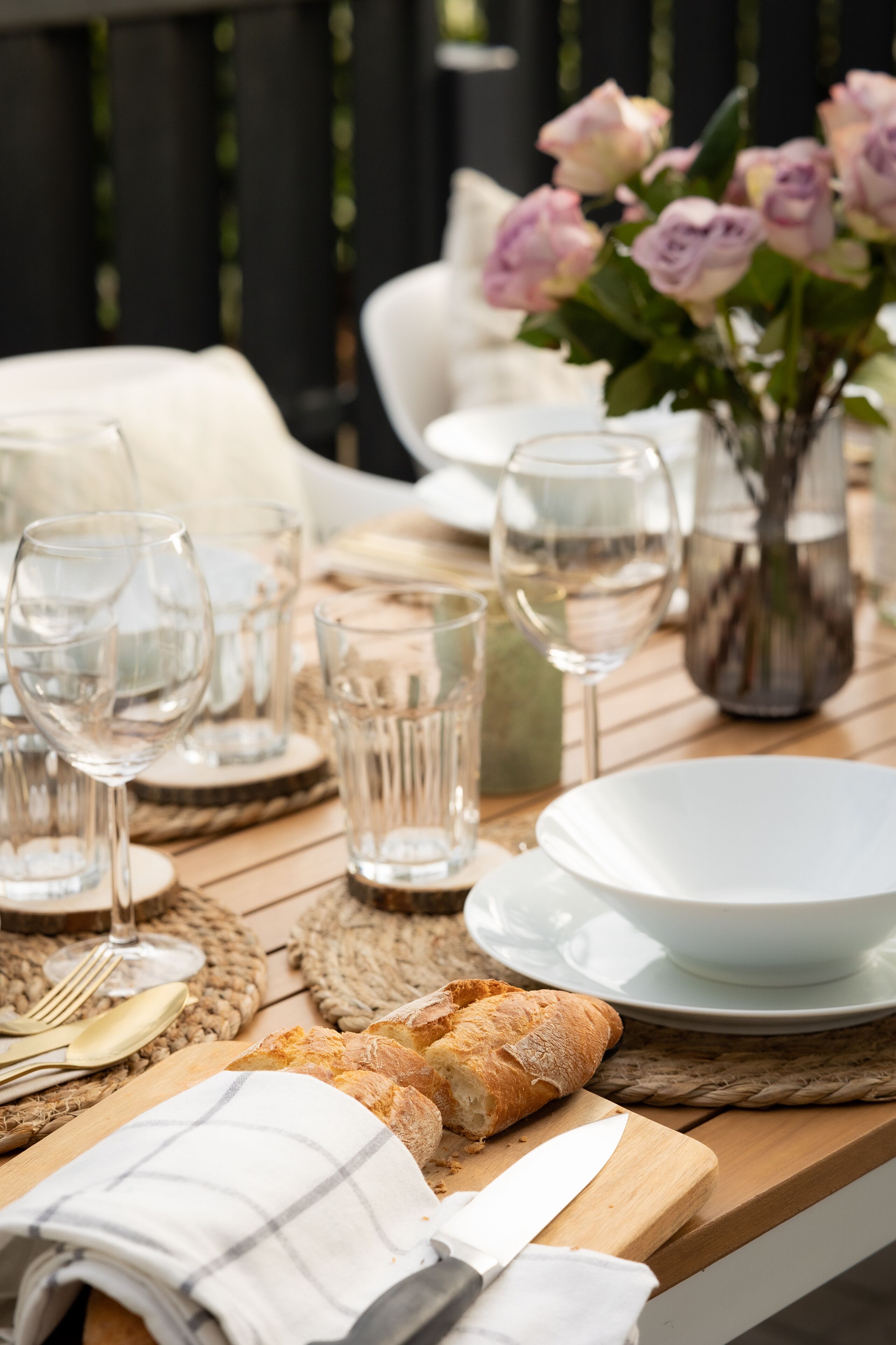Een houten tafel gedekt met glazen servies, een witte kom, een mes, een brood en een vaas met bloemen.