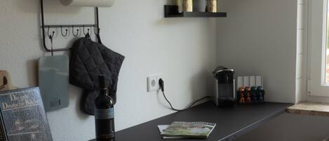 A kitchen with a wooden counter, a hanging rack with kitchen utensils, a potted plant, and a trash bin.