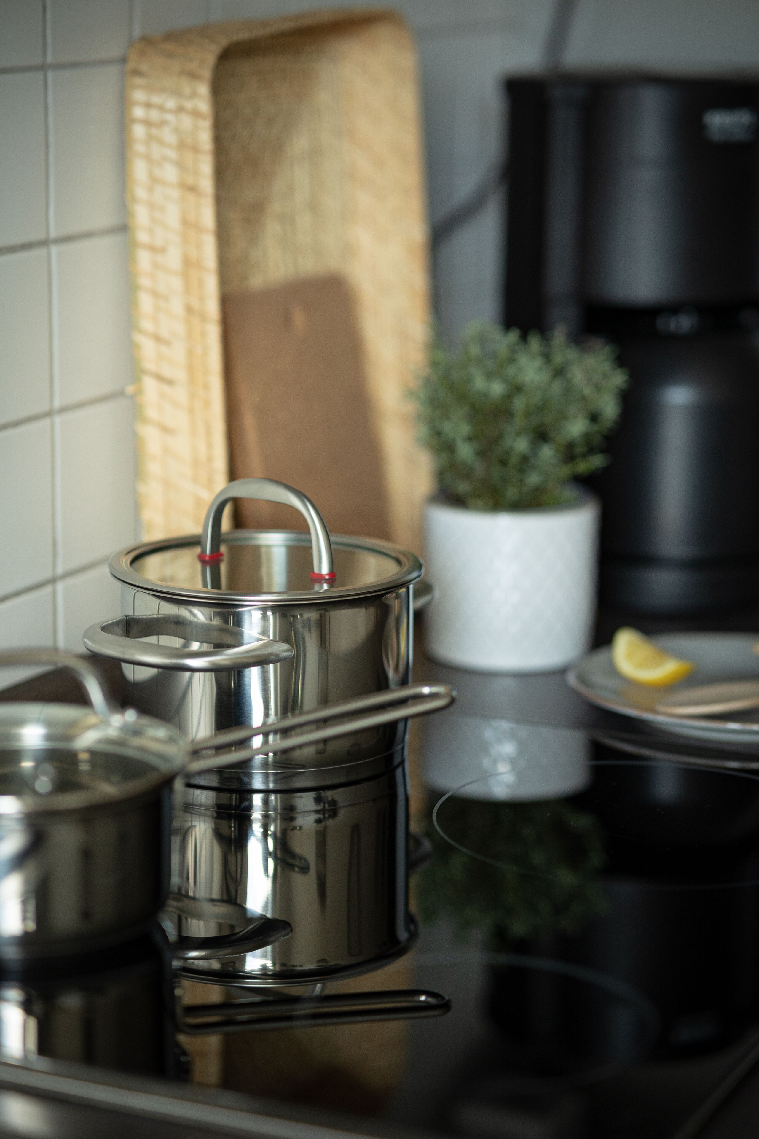Utensílios de aço inoxidável em uma bancada de cozinha, uma panela branca e uma cafeteira preta ao fundo.