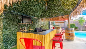 An outdoor bar area with a bamboo enclosure, red chairs, and a pool in the background.