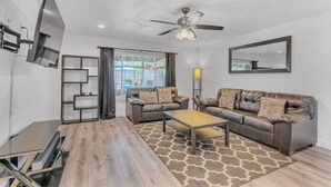 A modern living room with a sofa, coffee table, TV, and a ceiling fan.
