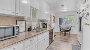 A modern kitchen with white cabinets, a granite countertop, a built-in microwave, a coffee maker, and a dining area with a table and chairs.