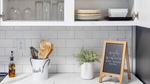 A kitchen with white cabinets, a marble countertop, and a chalkboard sign.