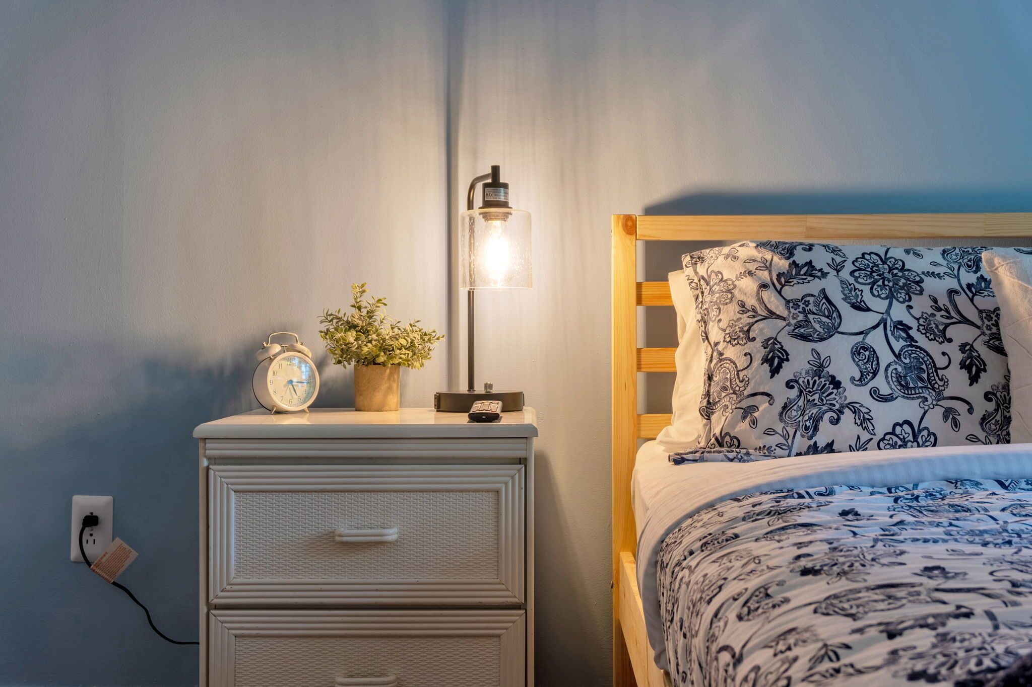 Une chambre à coucher avec un lit, une table de chevet avec une lampe, une horloge et une petite plante.