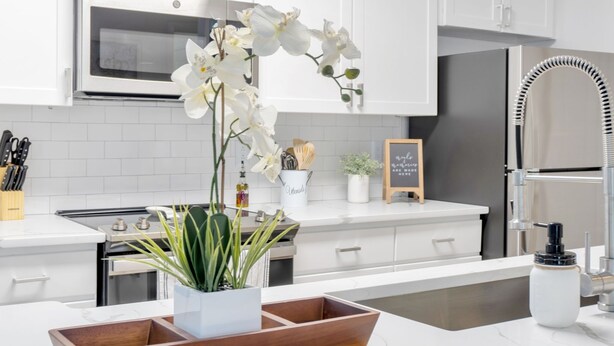 A modern kitchen with white cabinets, stainless steel appliances, and a wooden serving tray with a potted plant.