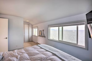 A bedroom with a large window, a bed, and a door leading to another room.