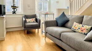 A cozy living room with a grey sofa, a matching armchair, and a wooden floor. - 2 bedroom accommodation in Beadnell, nr Chathill (Beadnell, nr Chathill)
