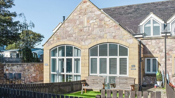 A stone building with large arched windows and a small garden area with wooden furniture. - 2 bedroom accommodation in Beadnell, nr Chathill (Beadnell, nr Chathill)