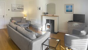 A modern living room with a fireplace, grey sofas, a glass coffee table, and a television on a cabinet. - 2 bedroom accommodation in Beadnell, nr Chathill (Beadnell, nr Chathill)