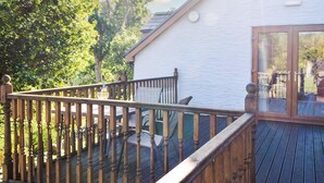 A wooden deck with a railing, a white building with a glass door, and a view of trees and sky. - 1 bedroom accommodation in Capel Dewi (Capel Dewi)