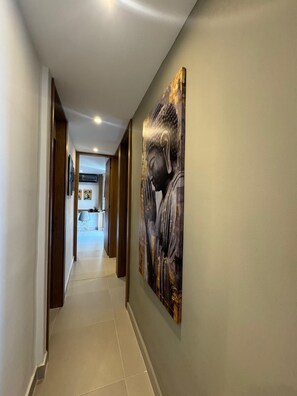 A hallway with a large Buddha painting on the wall, leading to a room with a desk and chair.