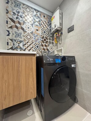 A compact laundry room with a front-loading washing machine, a tiled backsplash, and a wooden cabinet.
