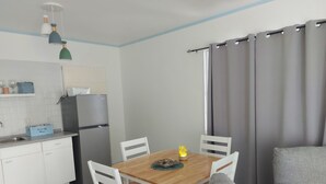 Een kleine leefruimte met een eethoek, kitchenette en een grijze bank.