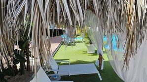 Een overdekt terras met witte loungestoelen en een zwembad op de achtergrond.