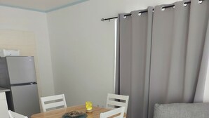 Een moderne woonkamer met een houten eettafel, witte stoelen, een grijze bank en een grijze fauteuil. Op de eettafel staat een kleine tafellamp.
