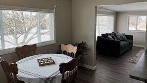 A dining area with a table set for four, a ceiling fan, and a view of a living room with a couch. - Cozy Stay Near National Parks & BYUI - Sleeps 6 (Rexburg)
