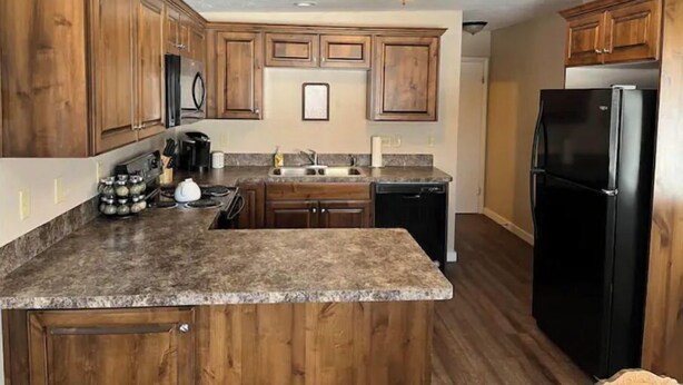 A kitchen with wooden cabinets, a granite countertop, a black refrigerator, and a microwave. - Cozy Stay Near National Parks & BYUI - Sleeps 6 (Rexburg)