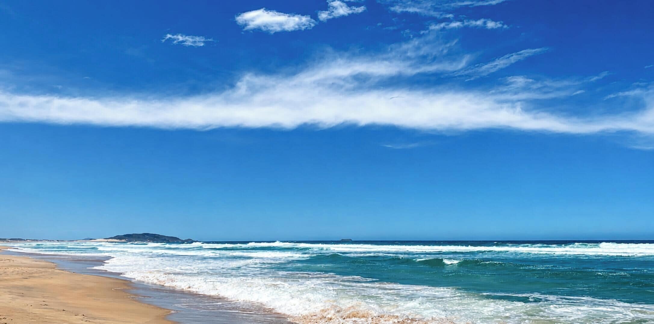A beach with waves, a clear sky, and a distant island.