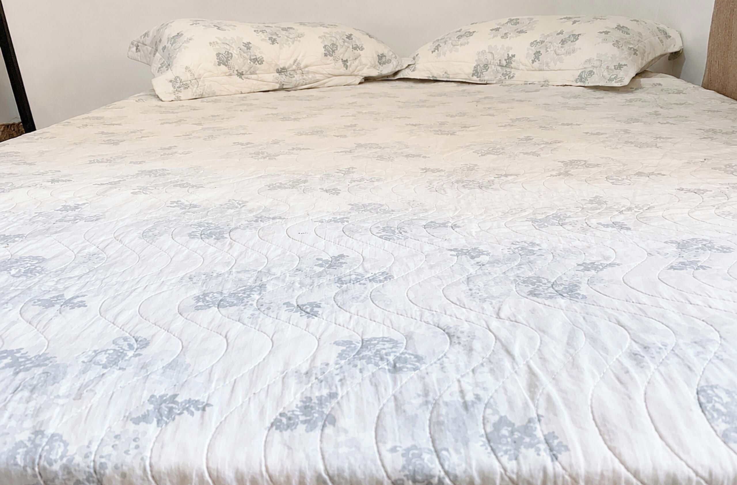 A bed with a floral patterned bedspread and two pillows.