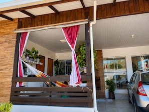 A covered outdoor seating area with a wooden bench and a hammock.
