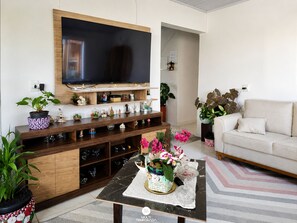 A living room with a flat-screen TV mounted on the wall, a wooden entertainment unit below, a beige sofa, and a coffee table with decorative items.