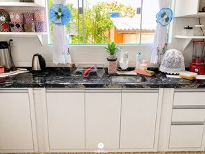 A kitchen with a granite countertop, stainless steel sink, and white cabinets.