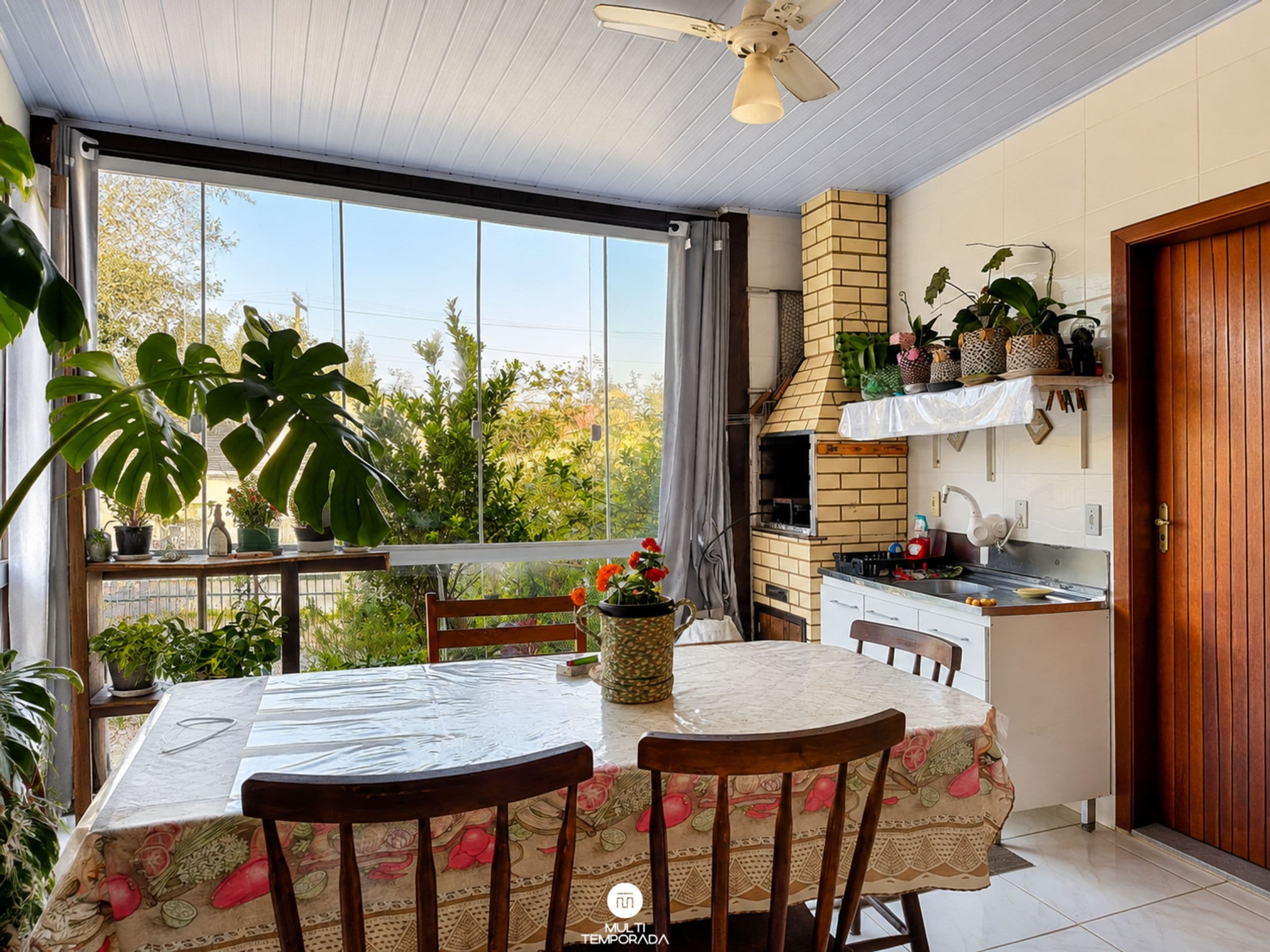 A kitchen with a brick oven, a dining table with chairs, and a view of greenery outside.
