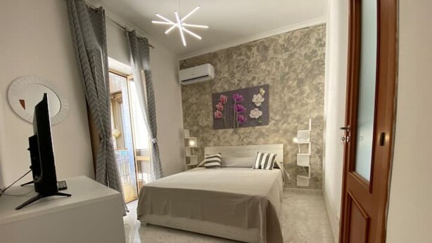 A bedroom with a bed, a TV on a stand, a wall-mounted air conditioner, and a decorative floral painting. - Sea and sun appartment whole accommodation (napoli)