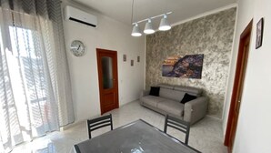 A living room with a sofa, a dining table, and a painting on the wall. - Sea and sun appartment whole accommodation (napoli)