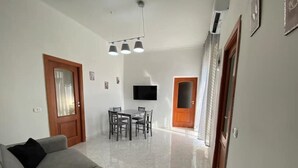 A living room with a sofa, a dining table with chairs, a TV mounted on the wall, and a door leading to another room. - Sea and sun appartment whole accommodation (napoli)
