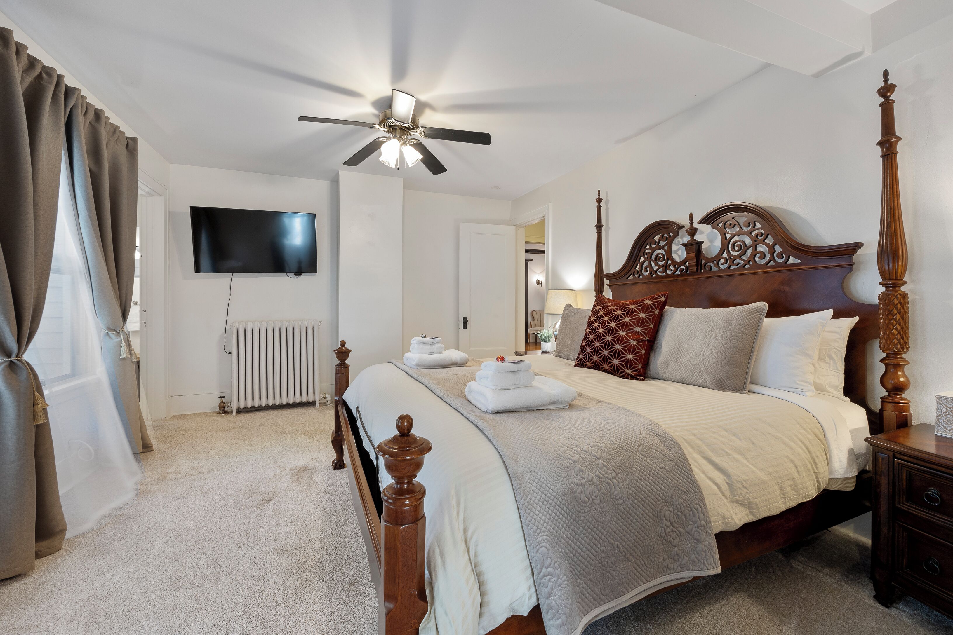 A neatly arranged bedroom with a four-poster bed, a ceiling fan, a flat-screen TV, and a radiator.