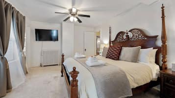 A neatly arranged bedroom with a four-poster bed, a ceiling fan, a flat-screen TV, and a radiator.