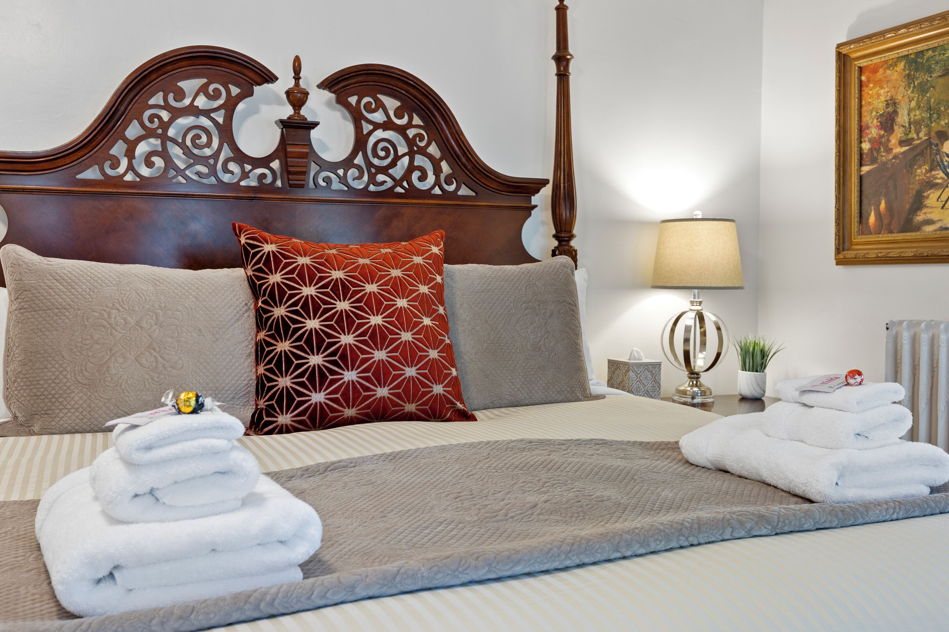 Uma cama bem arrumada com cabeceira decorativa, uma luminária de mesa e um quadro na parede.
