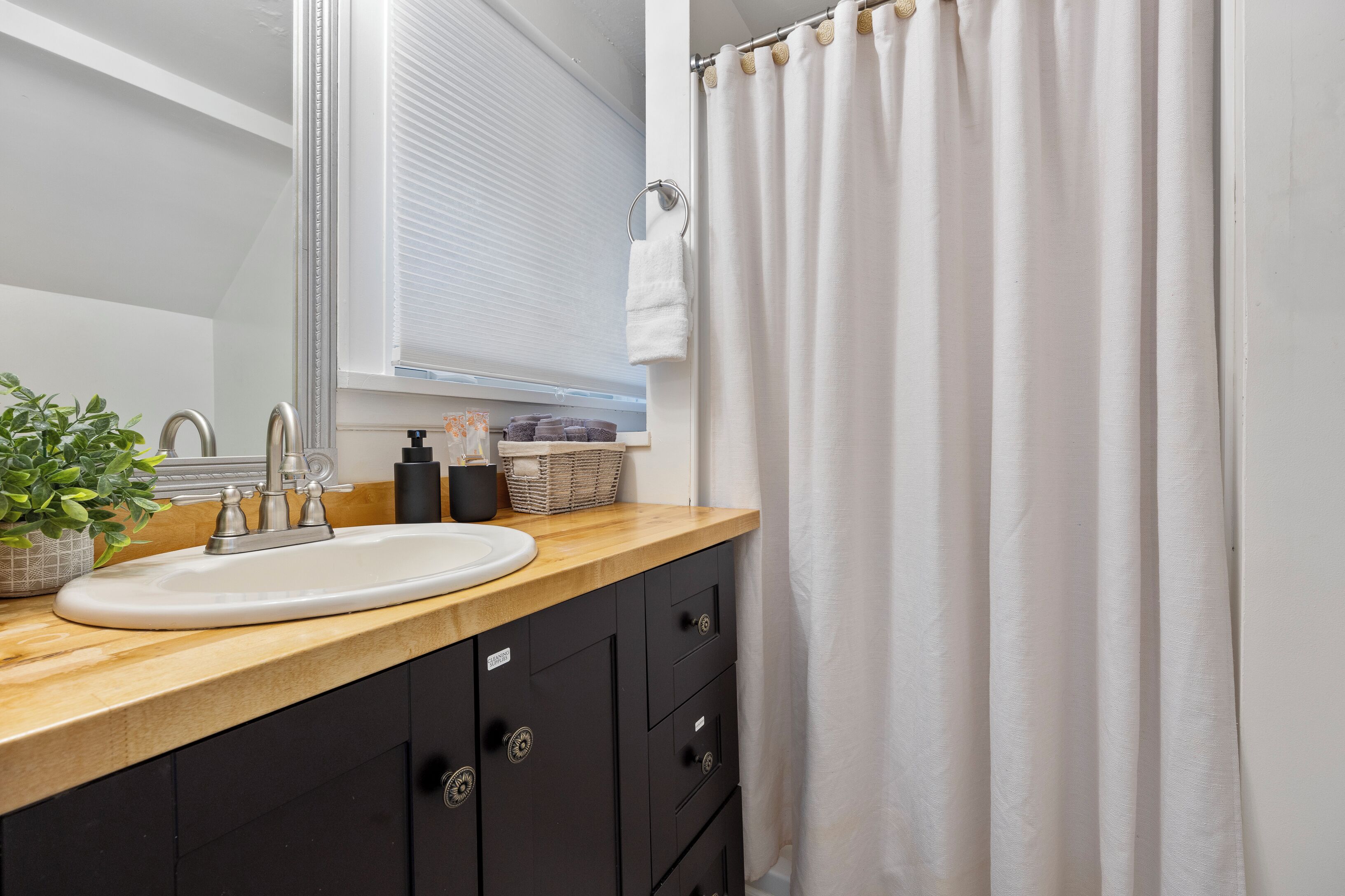 A bathroom with a wooden vanity, a white sink, a mirror, a towel ring, and a shower curtain.
