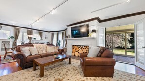 Een ruime woonkamer met een open haard, leren banken, een salontafel en een grote televisie.